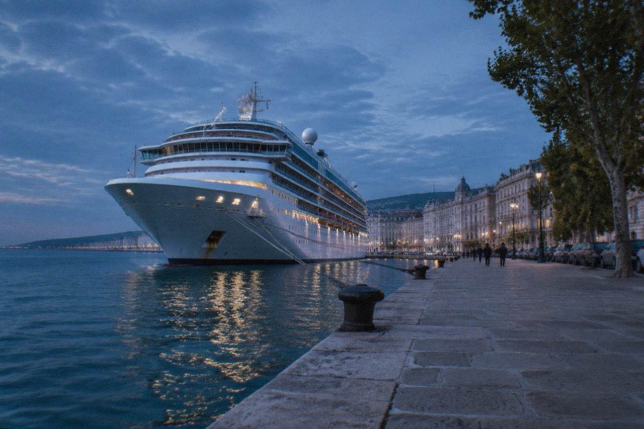 Cruise ship docked at Trieste's port with the city's seafront buildings behind it