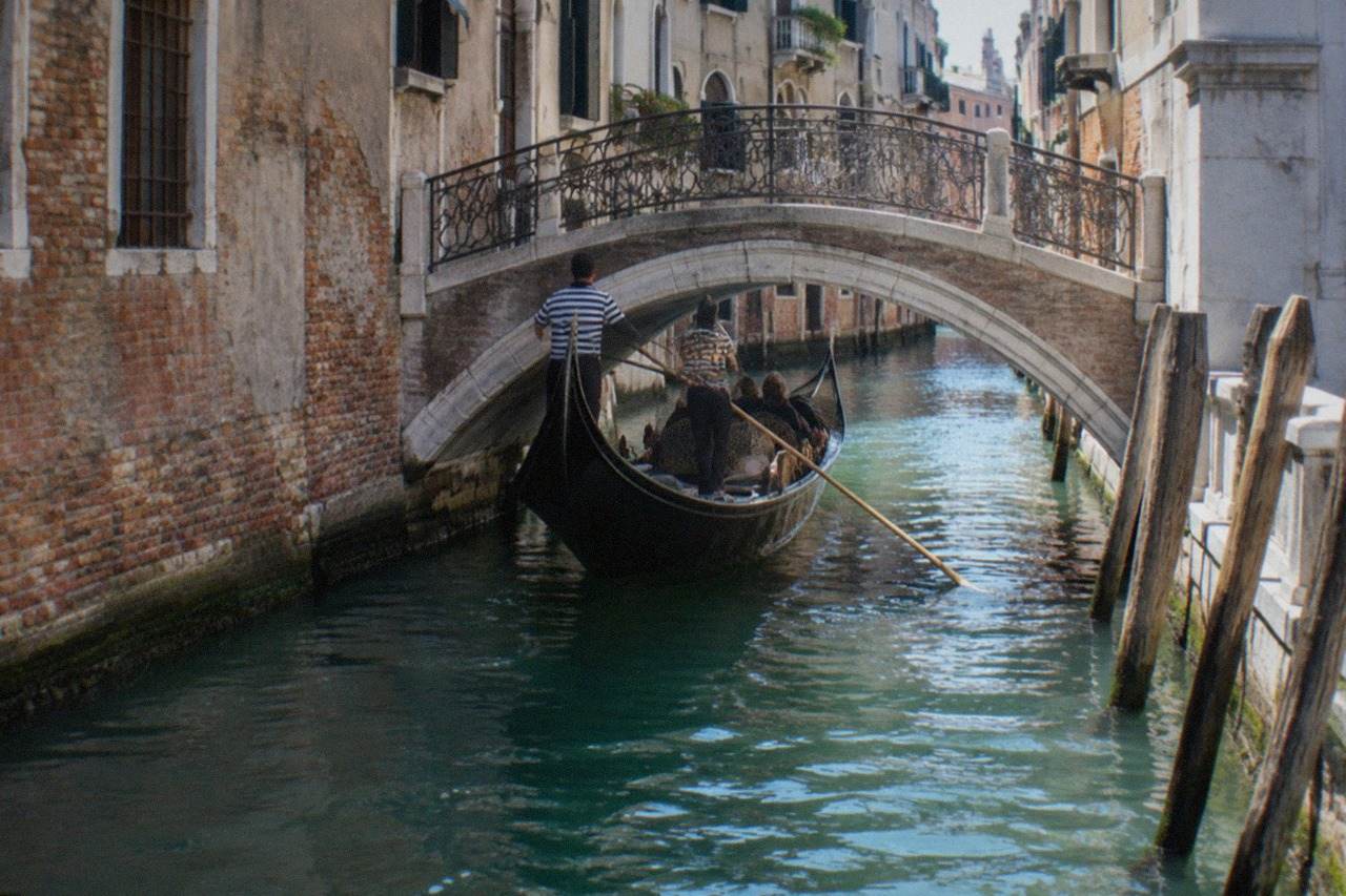 A Venice canal with a gondola passing under a small bridge between old palazzi