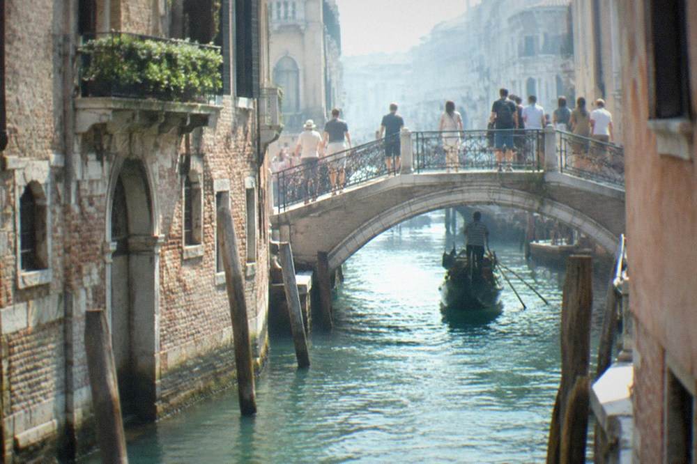 Crowds crossing a small arched bridge over a narrow Venice canal