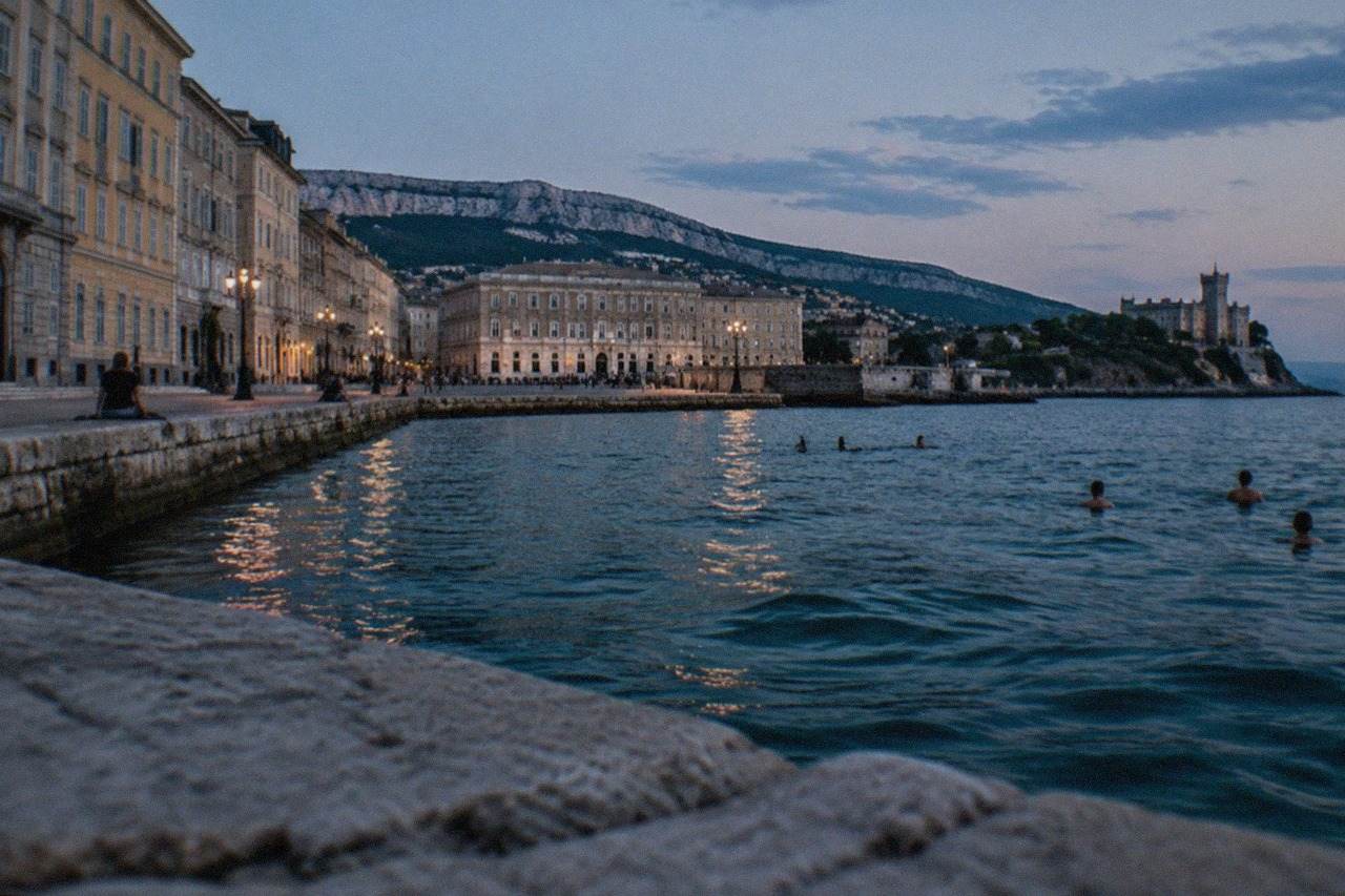 Swimmers in the sea along a stone waterfront with a castle on a headland in the distance