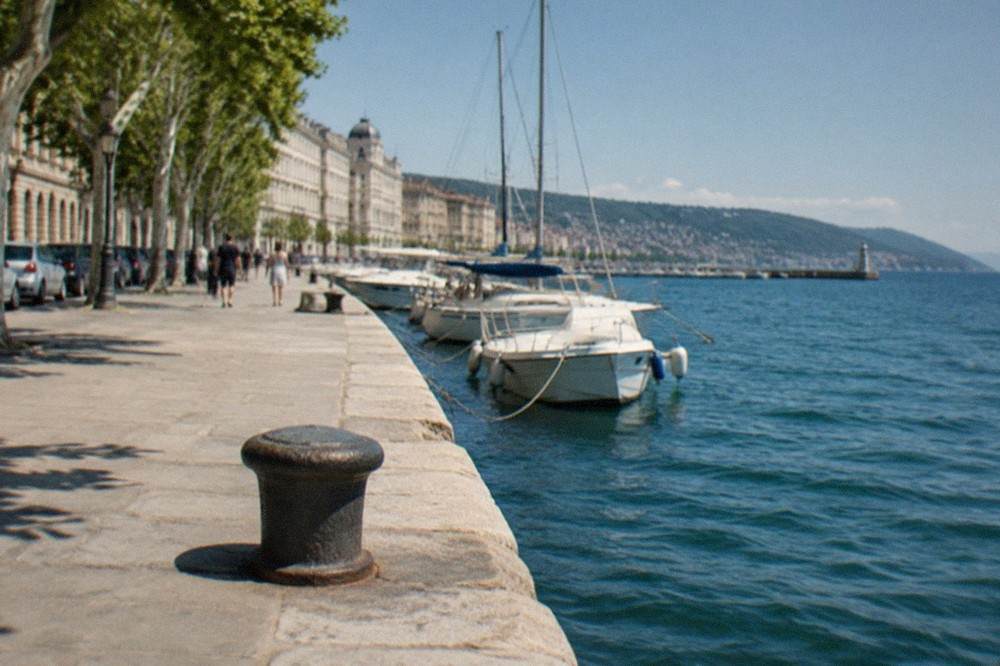 A view along the Trieste seafront promenade with calm blue water and a distant headland