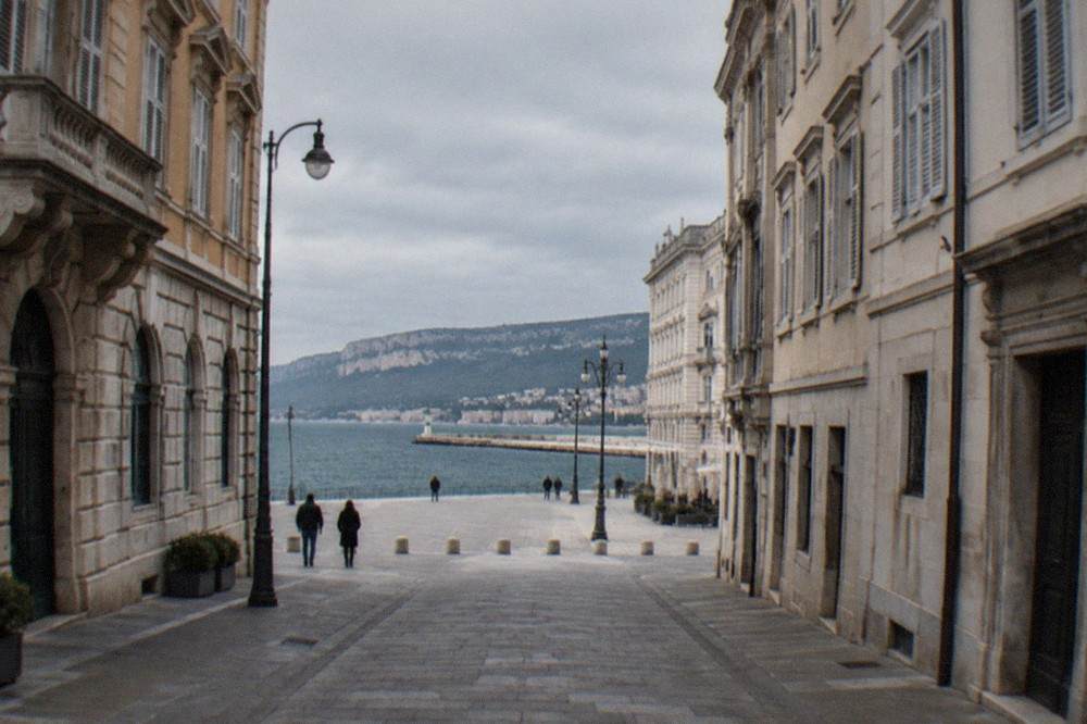 A narrow old-town street in Trieste with stone buildings and a view toward the sea