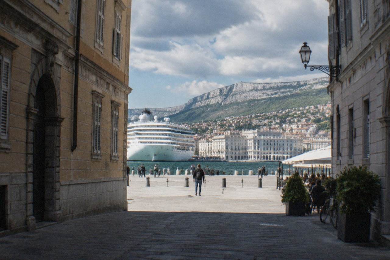 A cruise ship docked at the Trieste waterfront with the city's seafront buildings behind it
