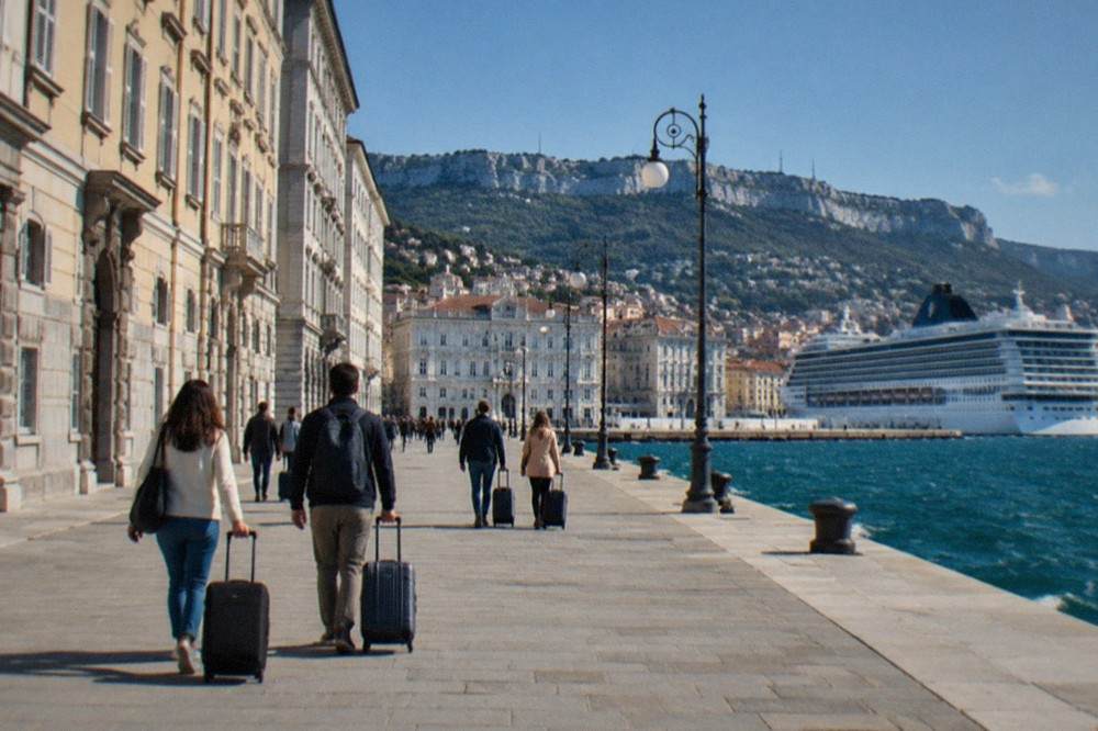 Travellers with suitcases walking along the Trieste seafront towards the cruise terminal on a bright morning