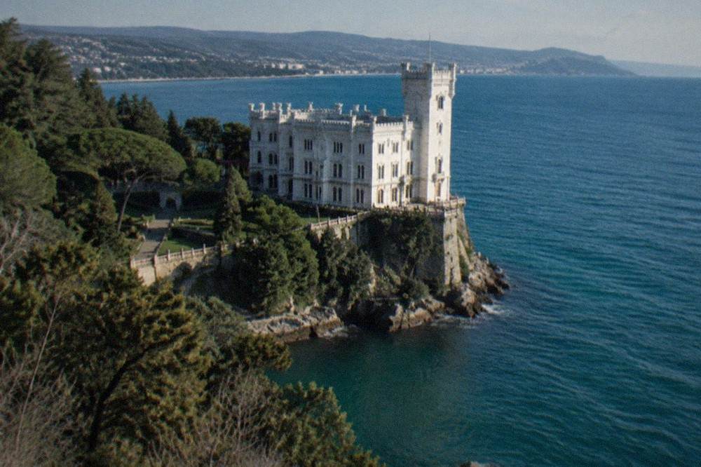 The white facade of Miramare Castle above its park with the Adriatic coastline beyond