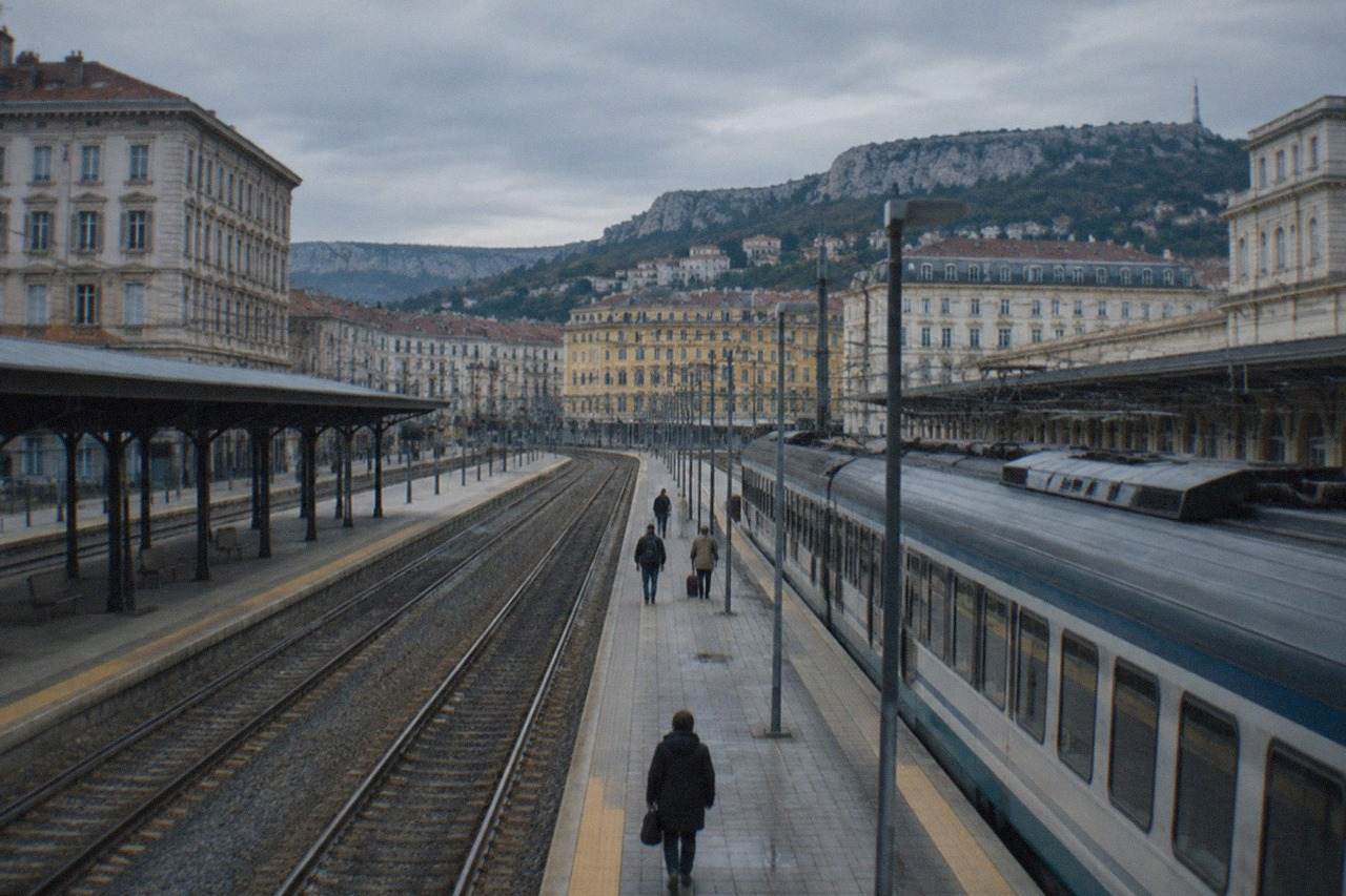 A passenger train standing at Trieste Centrale station under an overcast sky
