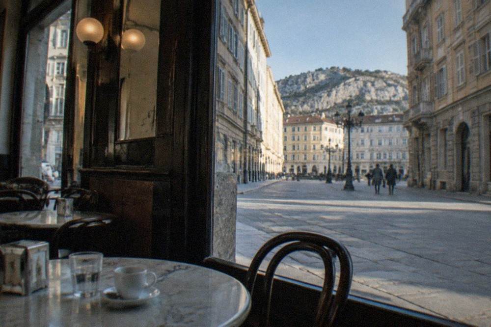 A historic Trieste caffè interior with marble tables and newspaper holders in the evening light