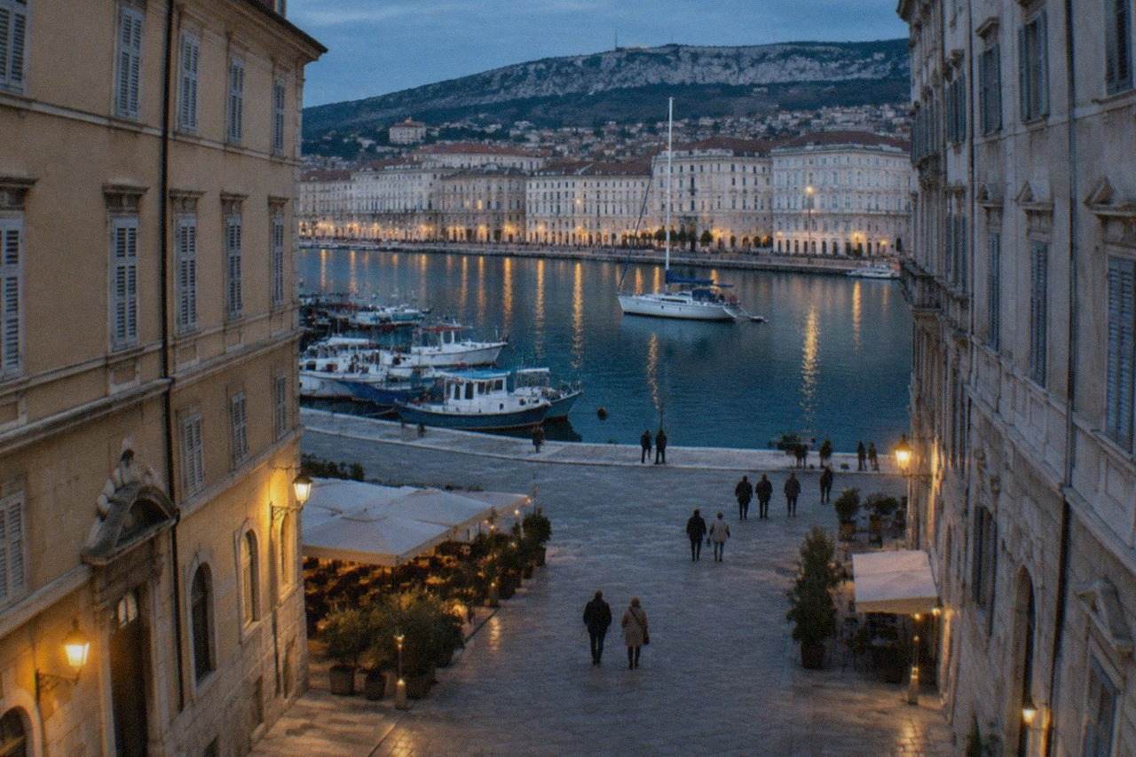 Fishing boats and a sailboat moored in the harbour of Trieste, Italy, with the seafront buildings behind them