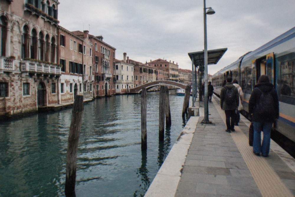 Passengers waiting on a platform beside a regional train at a small Italian seaside station