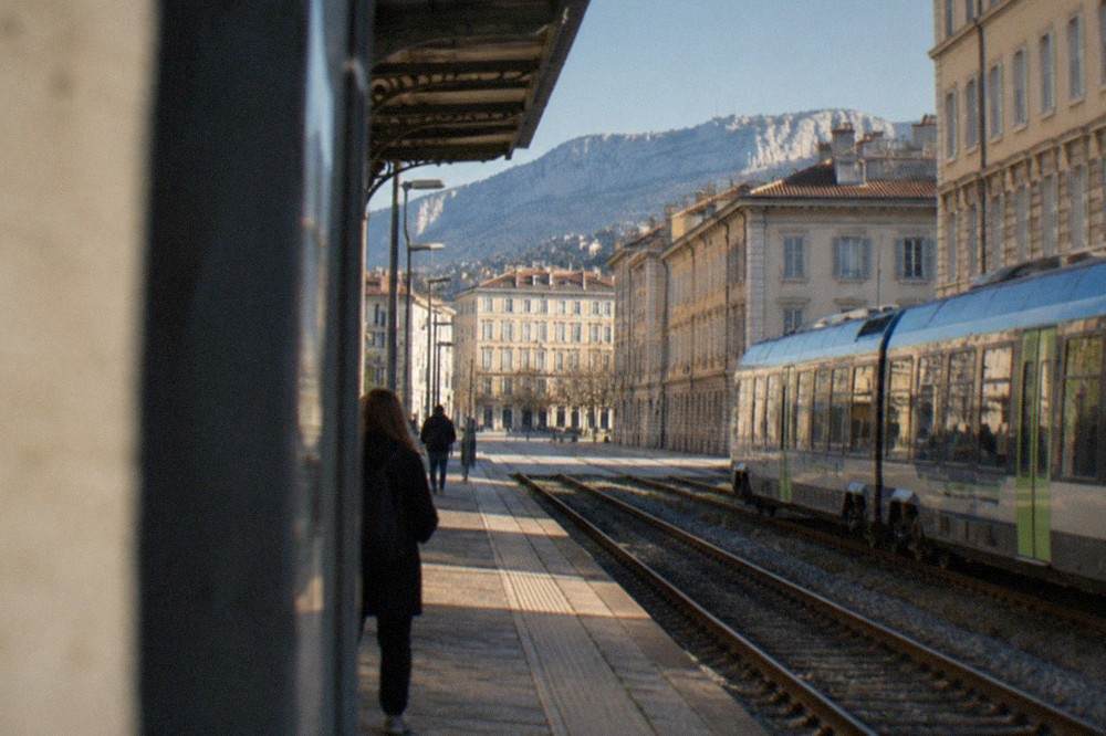 A regional train waiting at a small Italian railway station platform on a clear day