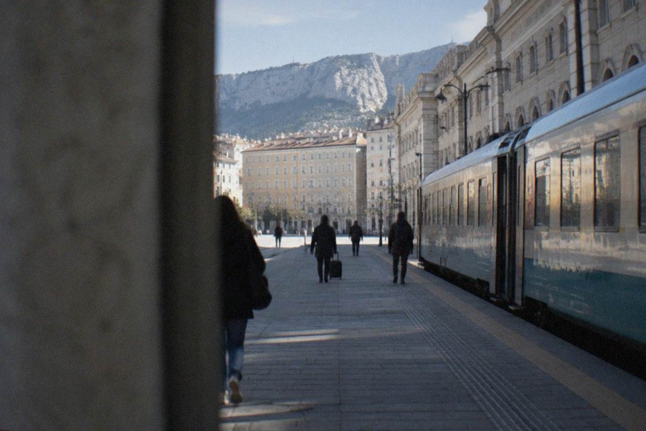 A passenger train standing at a platform beside a grand Italian railway station building
