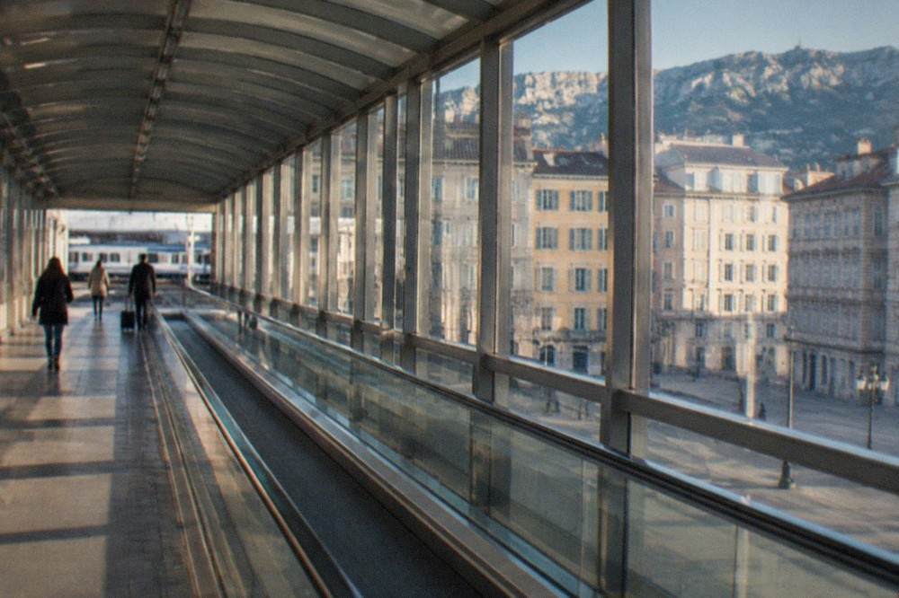 A covered airport walkway with moving walkways leading towards a small railway platform