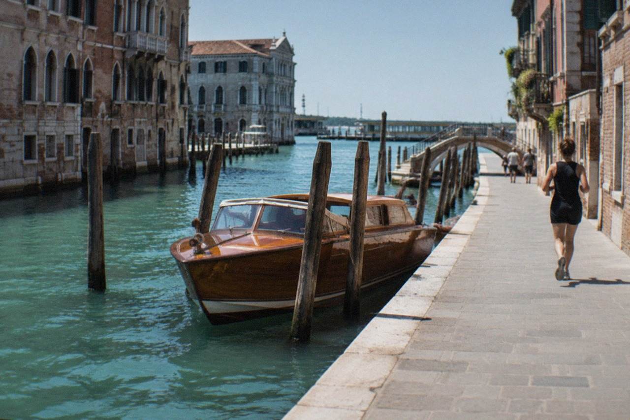 A wooden water taxi moored among the canals and old palaces of Venice, with a ferry terminal visible in the distance