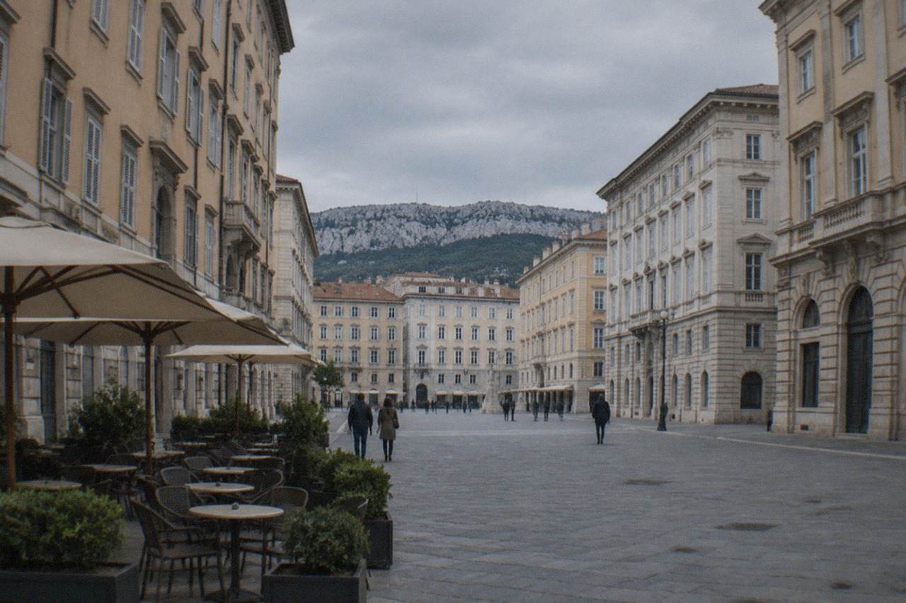 Tables and chairs outside a historic cafe on a wide square in Trieste, Italy