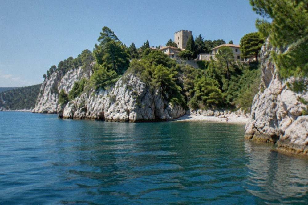 The white limestone cliffs and small pebble coves of the Duino coast near Trieste seen from the water on a calm summer morning