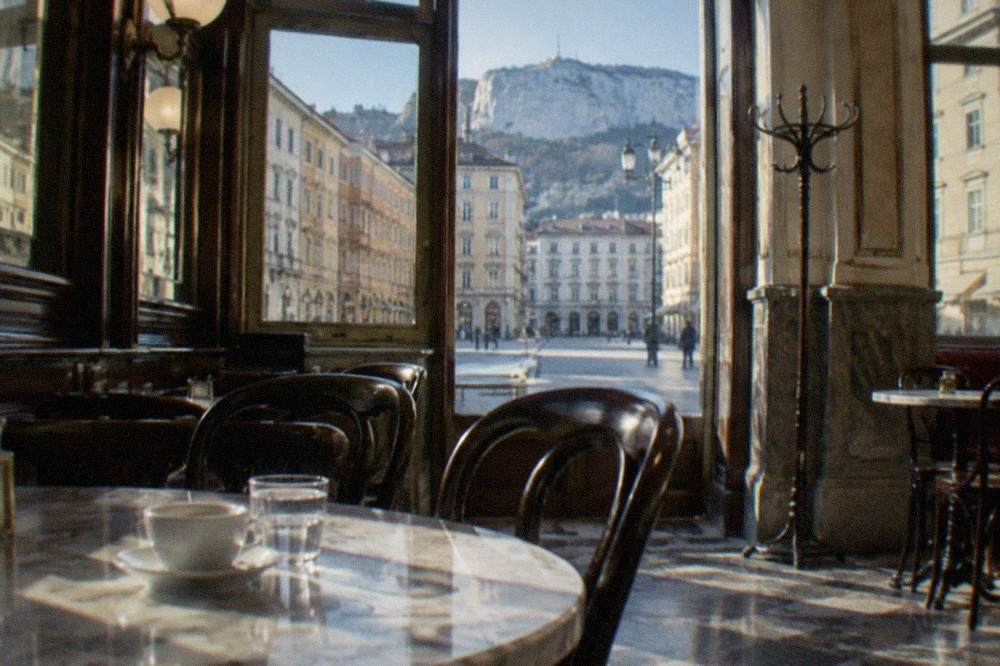 A historic Trieste coffee house interior with marble tables and newspaper readers