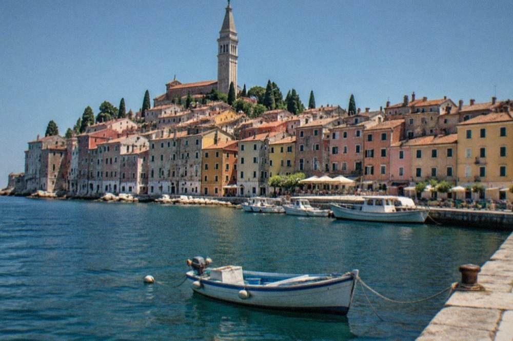 A small boat moored in a sheltered Adriatic harbour with stone quaysides and pastel buildings behind it