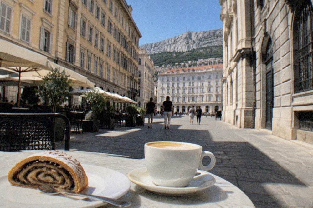 A slice of presnitz pastry beside a cup of coffee on a marble cafe table in Trieste