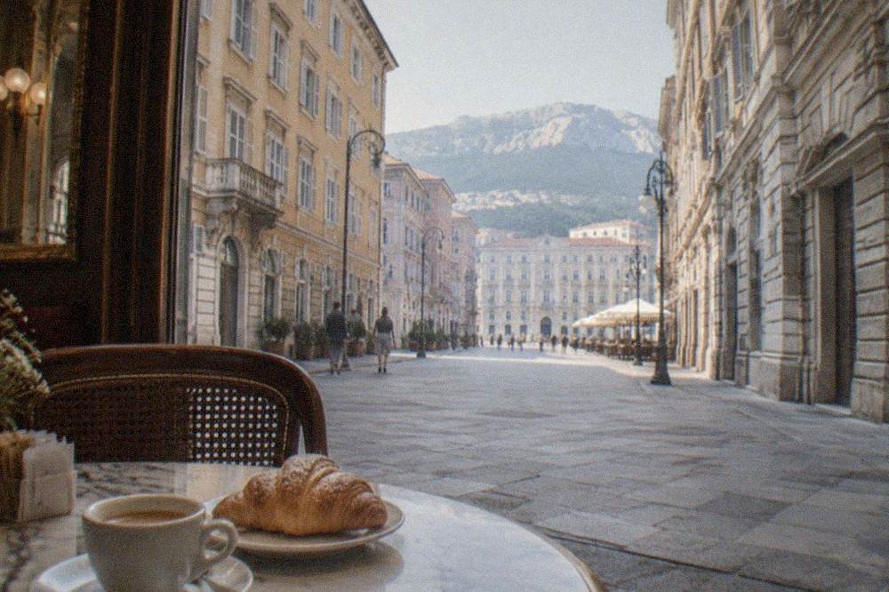 A cup of espresso with a pastry on a marble table inside an ornate historic Trieste cafe