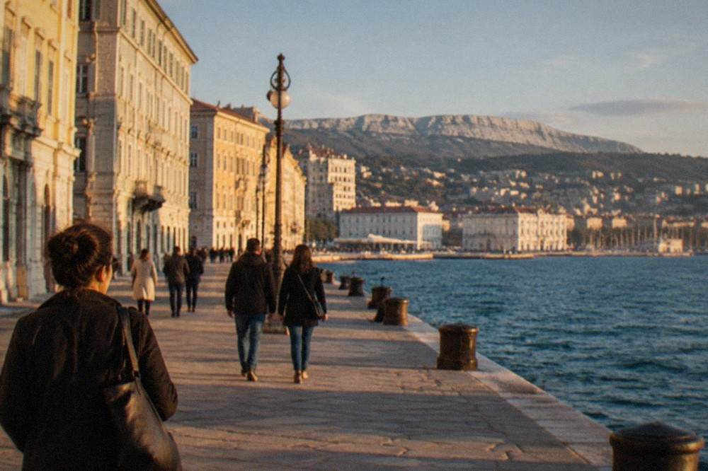 A seaside promenade in Trieste with people strolling beside the water