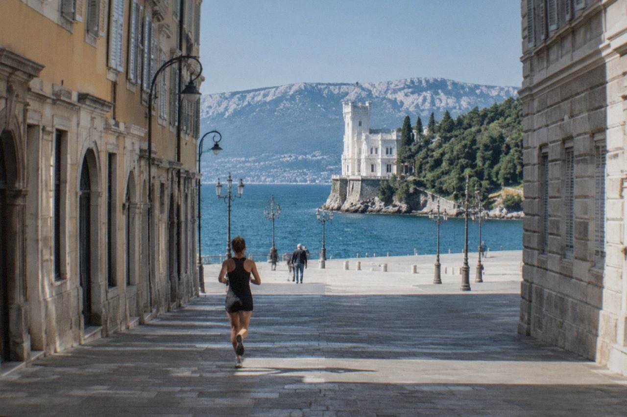 A white seaside castle on a rocky promontory above the Adriatic, with a wooded park behind it