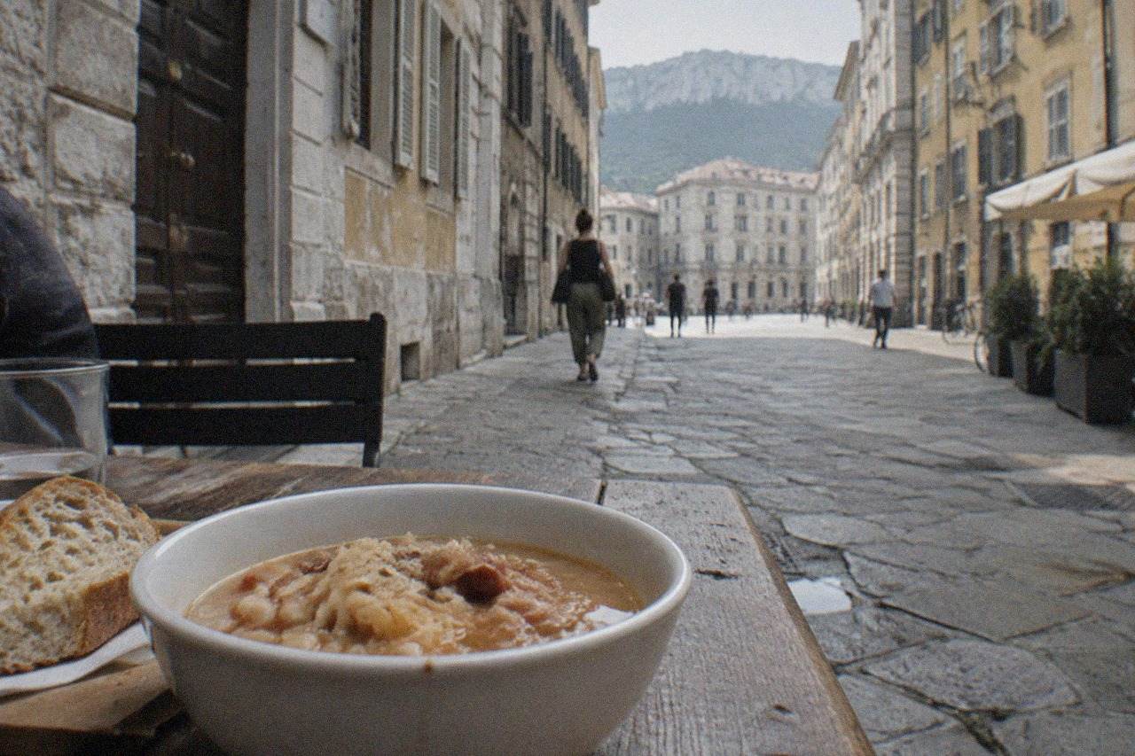 A bowl of Trieste jota soup with sauerkraut and beans beside crusty bread on a wooden table
