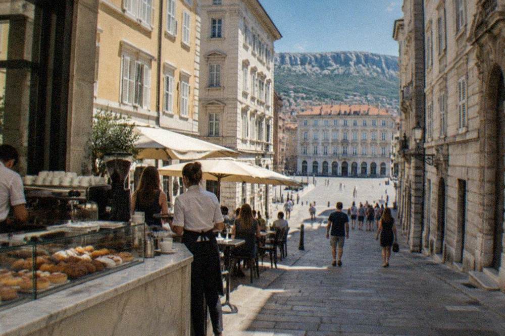 A marble cafe counter in Trieste with an espresso machine, pastries under glass and waiters taking orders