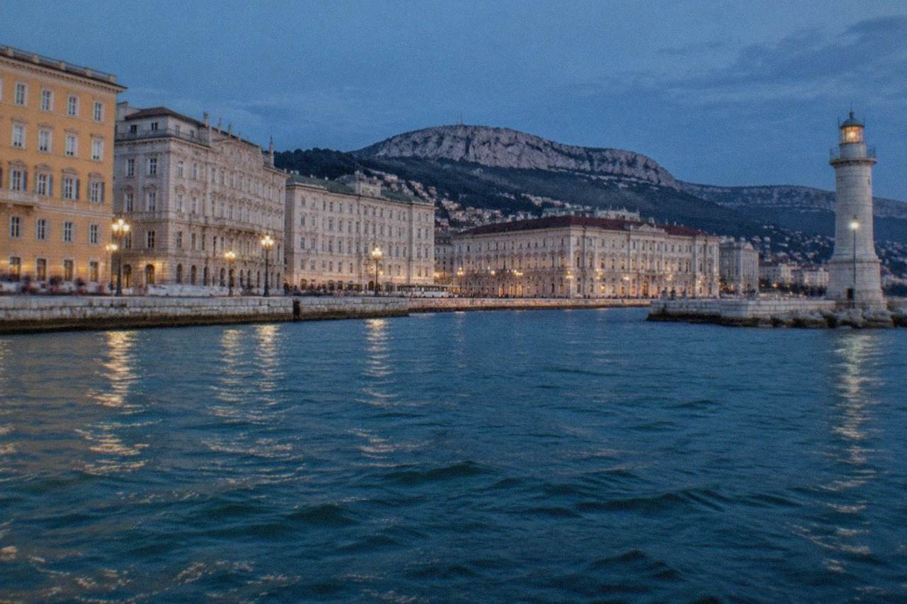 The seafront of Trieste, Italy seen from the water with the lighthouse and grand waterfront buildings along the Rive