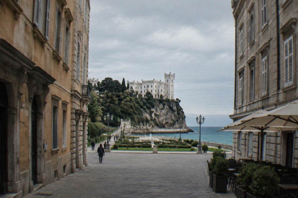 A white clifftop castle above the Adriatic with a formal garden in the foreground