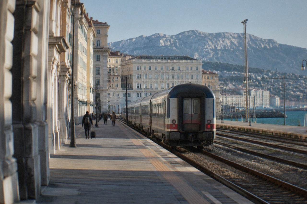 A passenger train beside the seaside platforms of Trieste Centrale station in Italy