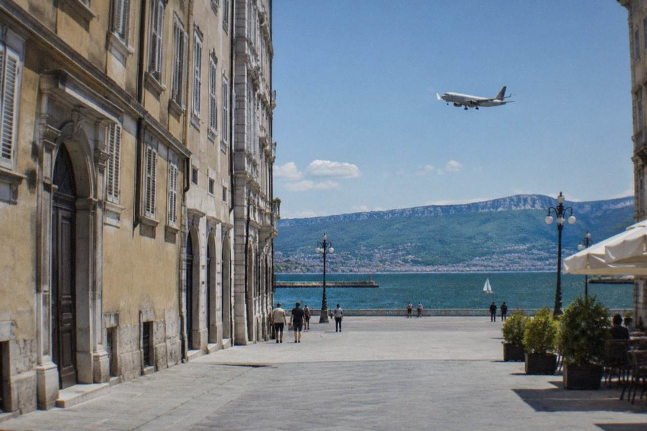 A passenger plane descending over the Adriatic coast toward Trieste Airport with the sea and hills below