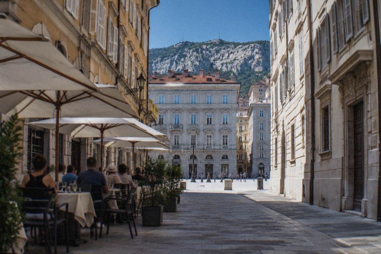 People eating at small tables outside a traditional buffet restaurant in a Trieste street