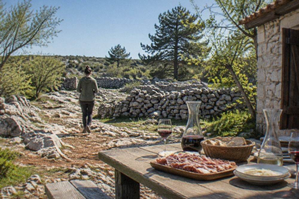 A farmhouse table set with carafes of wine and plates of cured meat at an osmiza on the Karst plateau