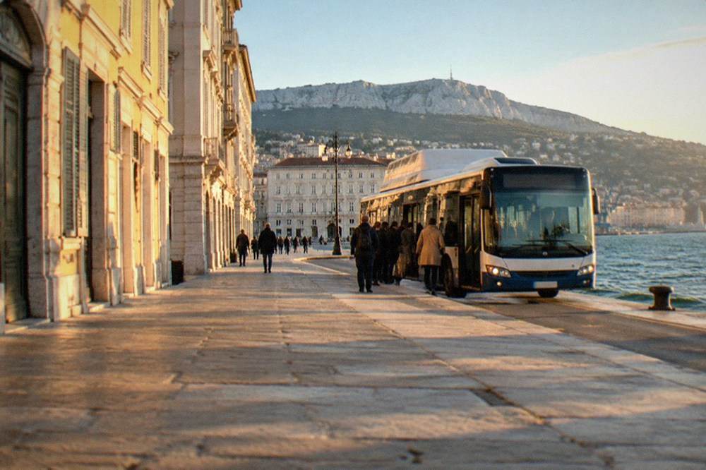 A Trieste city bus at a stop on the seafront with passengers boarding