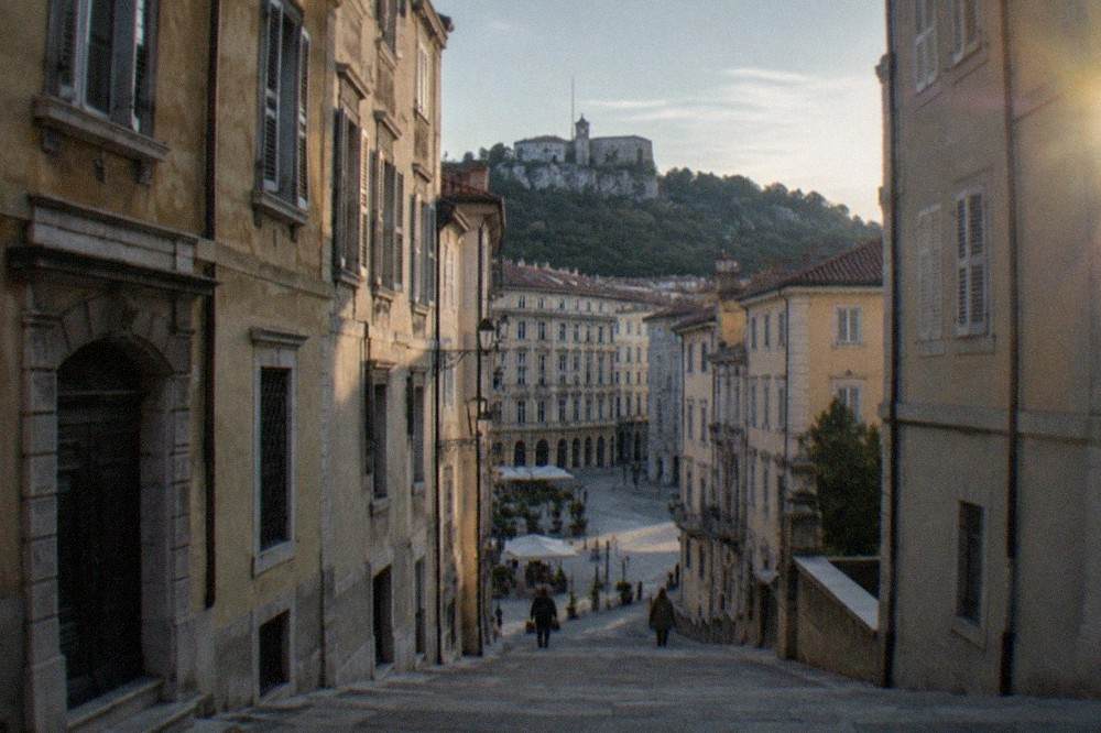 A quiet sloped lane in the old town of Trieste with older residential buildings rising toward the San Giusto hill