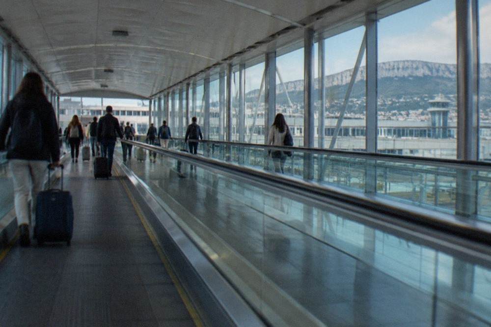 The covered walkway connecting Trieste Airport terminal to its railway station, with moving walkways and travellers with luggage