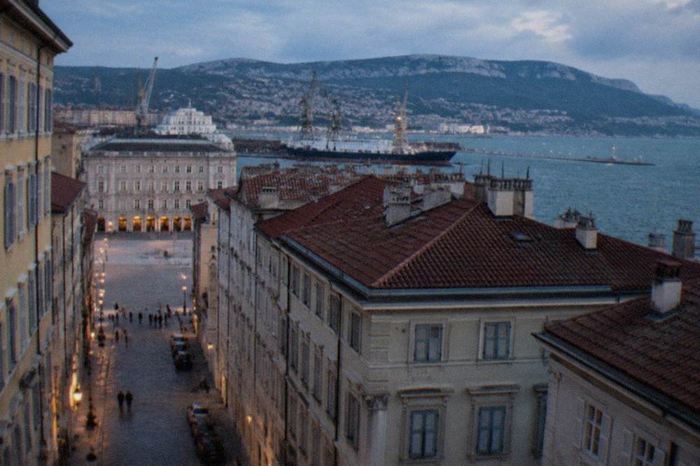 A view over the rooftops and harbour cranes of Trieste, Italy toward the hills that mark the Slovenian border