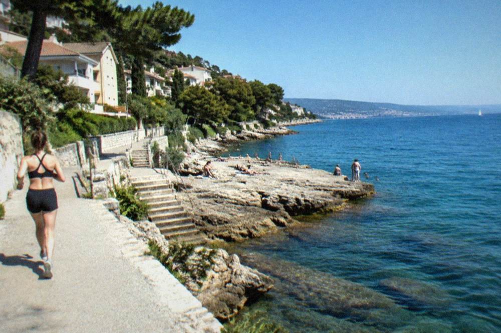 Bathers on a rocky platform at the Barcola shoreline with clear water below