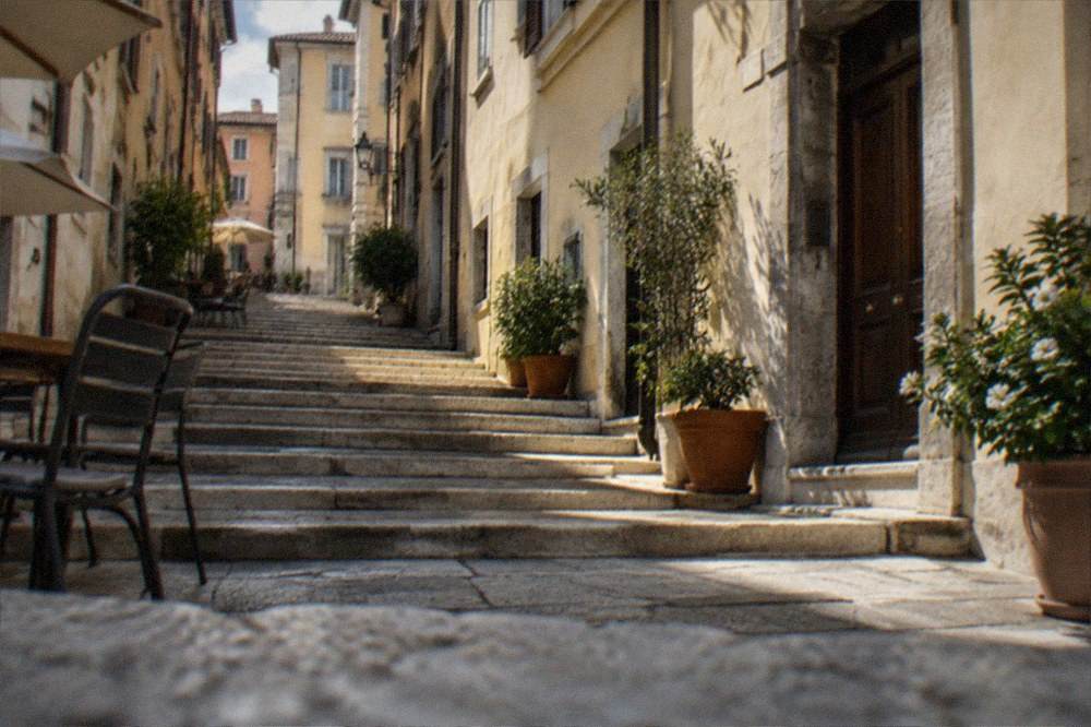 Sunlit stone staircase street in the Cavana district of Trieste with potted plants outside a doorway