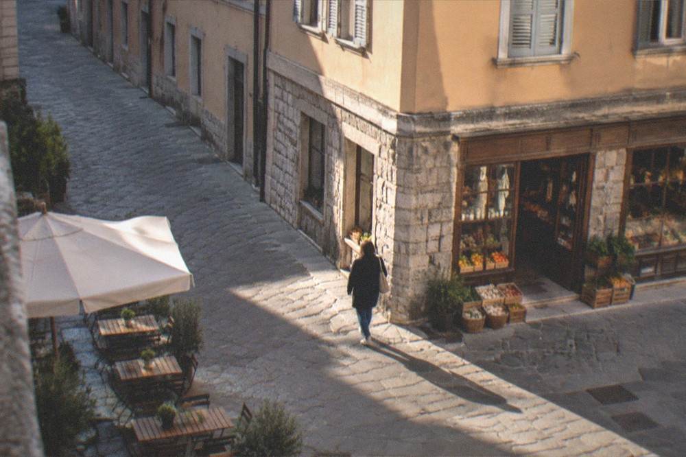 Morning light on a Cavana street corner in Trieste with a person walking past an old grocer's shopfront