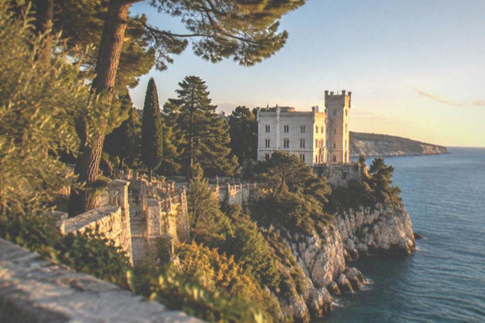 A white castle beside the sea with a park of trees and a terrace overlooking the water
