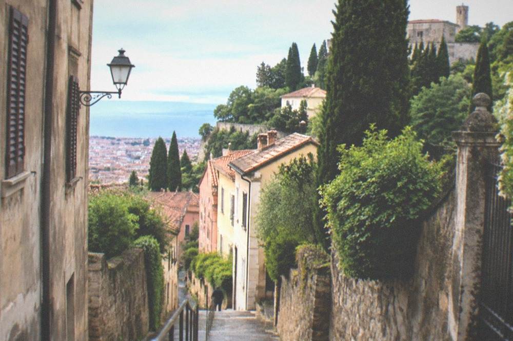 A stone staircase rising between old houses toward the San Giusto hill in Trieste