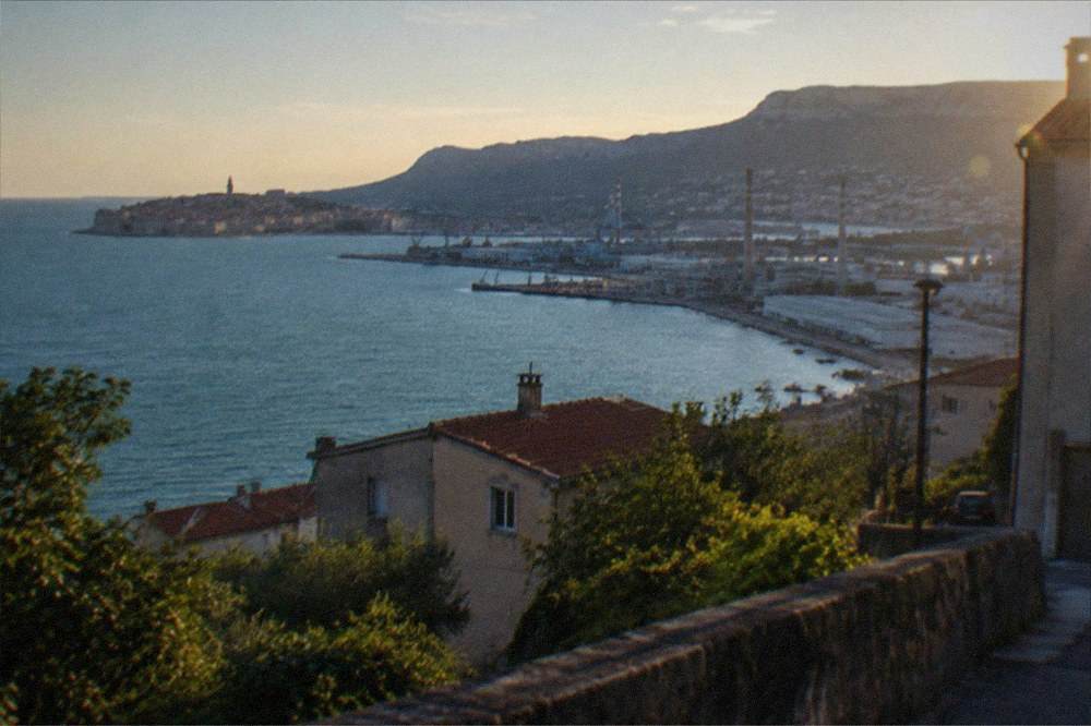 A walled seaside town on a peninsula seen from the water with terracotta roofs