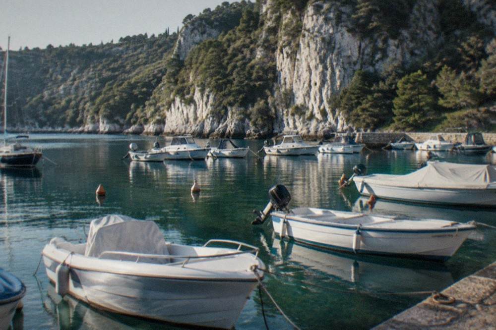 Small boats moored in a marina inside a sheltered bay with wooded cliffs behind