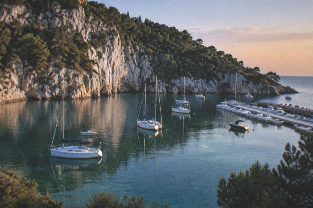A quiet bay at dusk with calm water, moored boats and dark pines against a fading sky