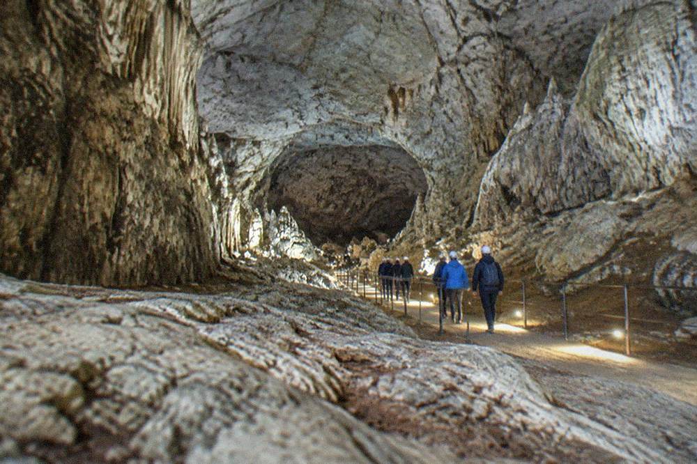 Visitors in helmets walking down a lit path inside an enormous limestone cave chamber