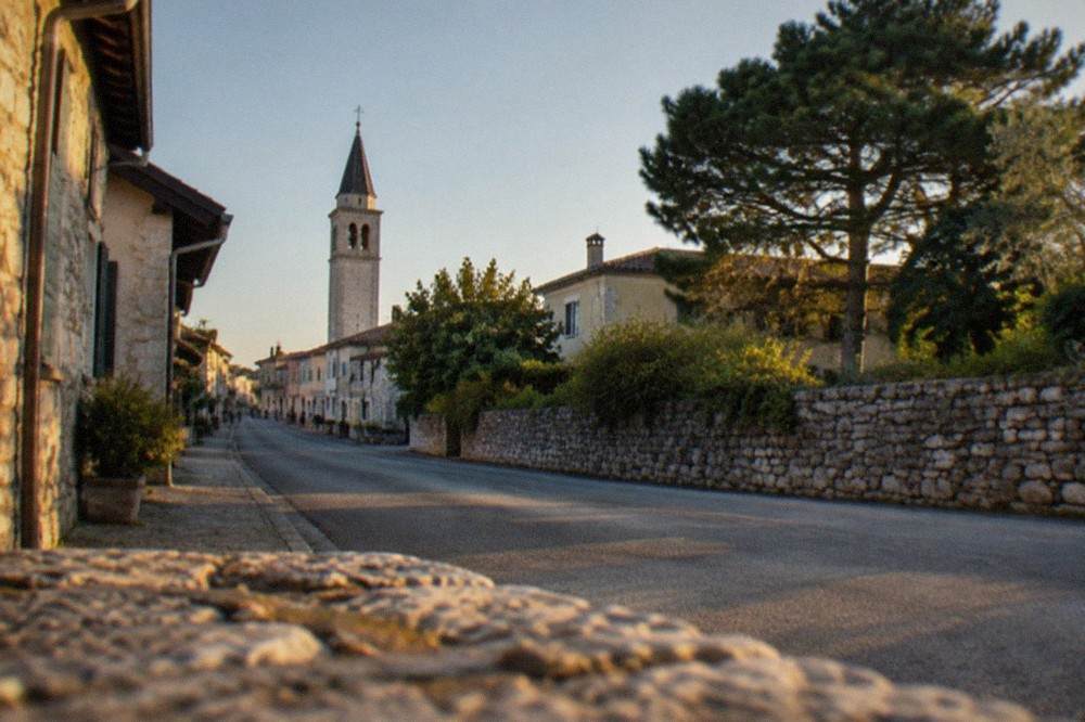 A village street lined with stone houses and a church tower under a clear sky