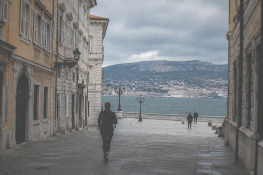 A stone terrace overlooking a gulf with a city on the shoreline and hills across the water