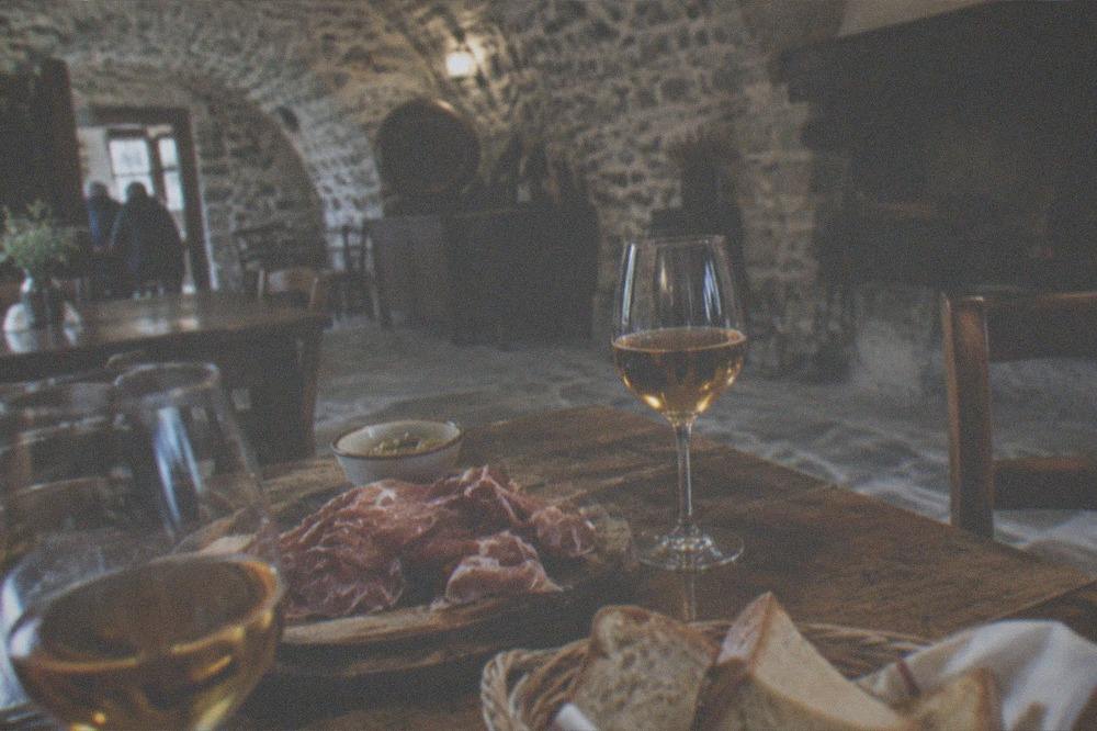 A rustic tavern table set with glasses of amber wine, cured ham and bread in a farmhouse cellar