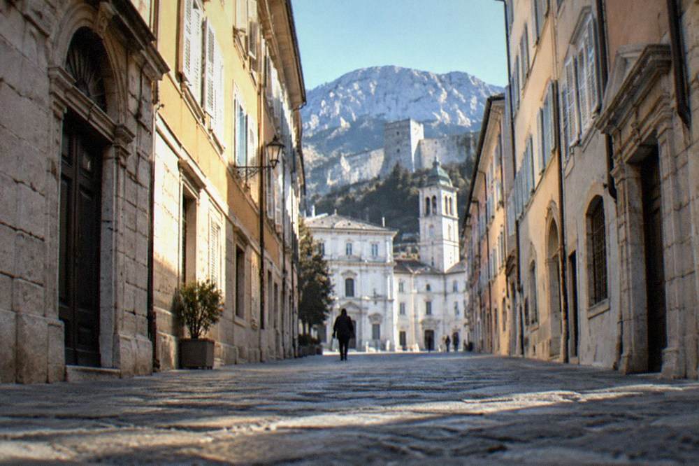 A narrow old-town street in Trieste sloping upward toward a stone castle and cathedral tower